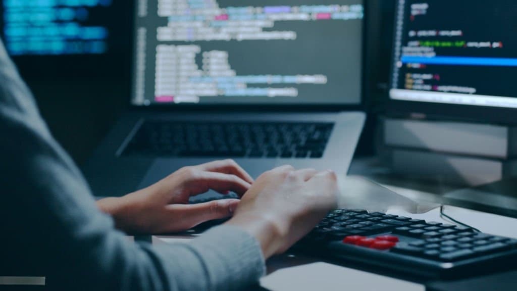 Developer working at keyboard with code on monitors